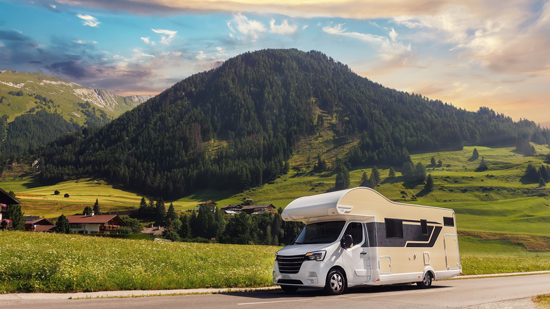 RV traveling on a road next to a tree-covered hill