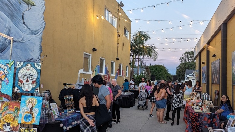 An alleyway with string lights hung over an art walk with shoppers browsing the stands