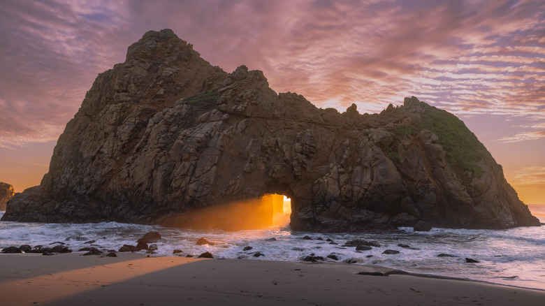 The orange glow of sunset shines through naturally formed Keyhole Arch on Pfeiffer Beach