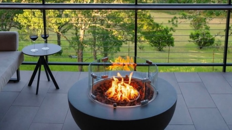 A roaring fire on a private balcony with two glasses of red wine overlooking trees and grass.
