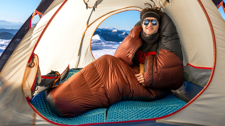 Camper warming up inside his tent and sleeping bag
