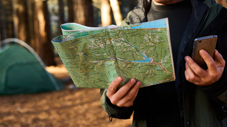 Camper holding a mobile phone and a map with tent in the background