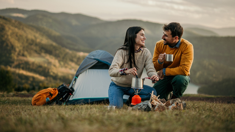 A happy couple drinking coffee in front of a tent.