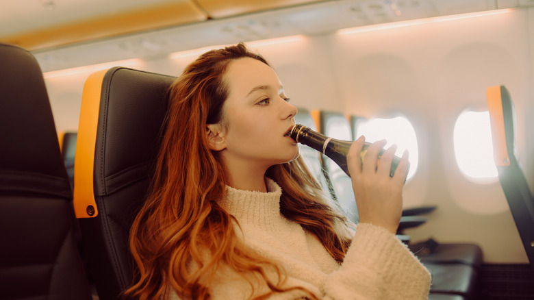 A girl in a plane drinks champagne from a small bottle