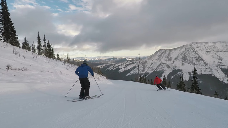 Two skiers make their way downhill at Castle Mountain Ski Resort, with a beautiful view of snowy mountains ahead