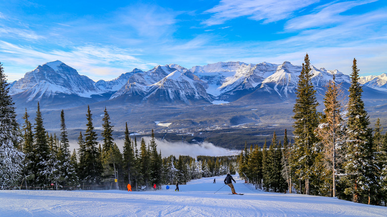 Skiers make their way down a run, with mountain peaks visible in the distance