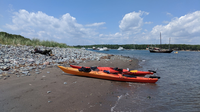 Kayaks beached on the shore of McNabs Island in Nova Scotia with boats in background