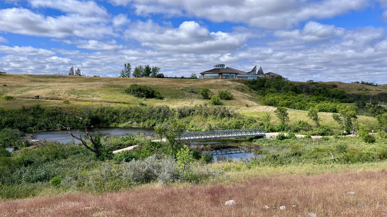 Bridge over creek in grassland, with Wanuskewin Heritage Park visitor center behind