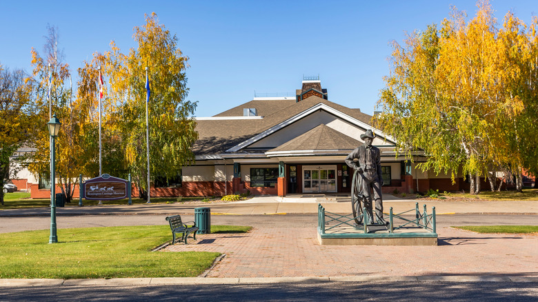 A statue of a cowboy stands in front of a single-story building on a sunny fall day