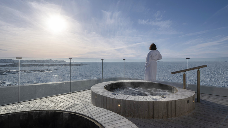 Woman looks over the Atlantic Ocean in front of the rooftop hot tubs at Fogo Island Inn, a hotel in Newfoundland and Labrador in Canada