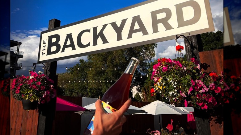 Person hold glass bottle in front of The Backyard brewery patio in Penticton.