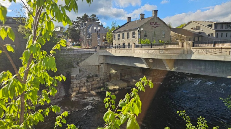 View of a bridge and historic gray stone building in Fergus, Ontario with greenery in the foreground