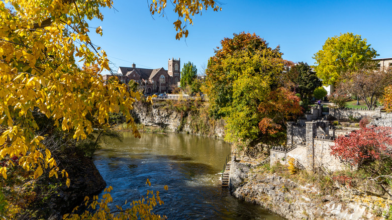 Autumn foliage in the trees lining the banks of the Grand River in Fergus, Ontario with a Scottish-style building in the background