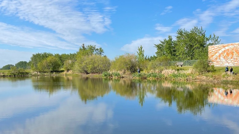 A tree-lined pond reflecting the blue sky with clouds in Centennial Park in Legal, Canada