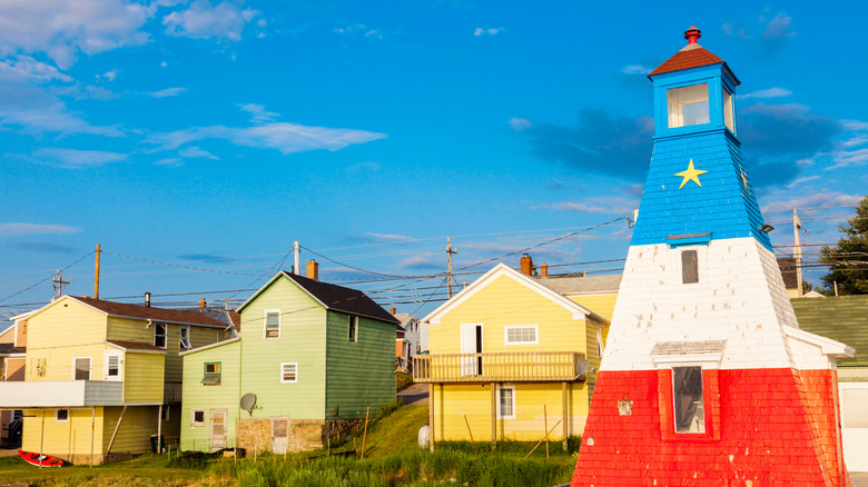 A blue, white, and red lighthouse next to pastel houses on the harbor in Chéticamp, Nova Scotia