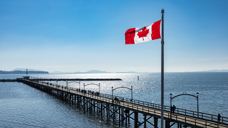 A Canadian flag flying above White Rock Pier, with people strolling on the pier