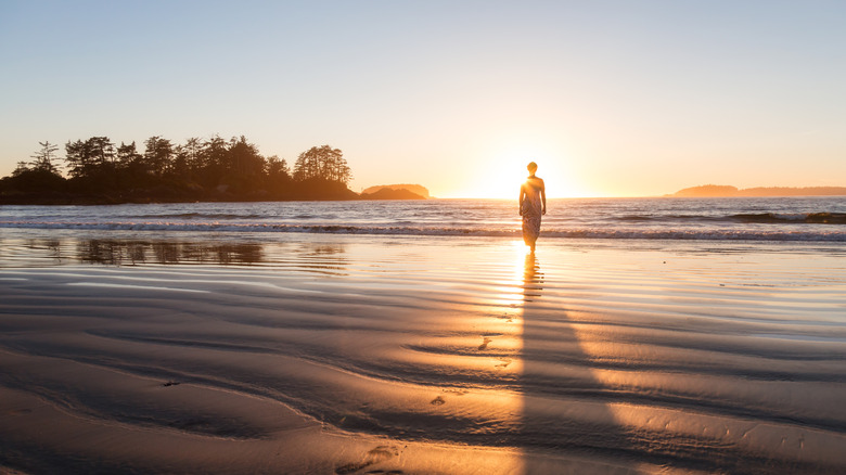 A woman is silhouetted against the sunset as she walks on Chesterman Beach in Tofino, Vancouver Island, British Columbia, Canada