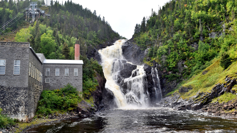 The rushing Ouiatchouan Falls and Ouiatchouan River beside the old pulp mill in in the historic village of Val-Jalbert, with a view of the cable car line going up the hill in the background