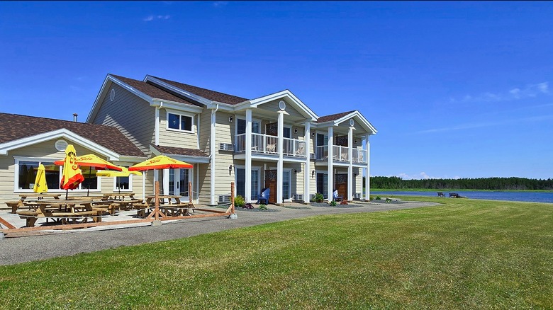 The Malia Spa and Resort on a sunny, blue-sky day, with outdoor seating on the patio, green grass, and the water visible behind it