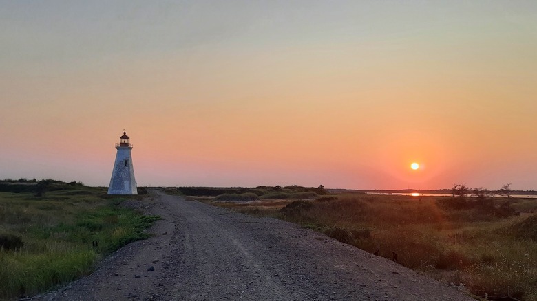 An old lighthouse on Lamèque Island at sunset, with a gravel road running off into the distance lined on either side with grass