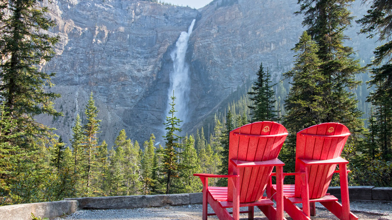 Two red Adirondack chairs stand in front of Takakkaw Falls in Yoho National Park, Canada