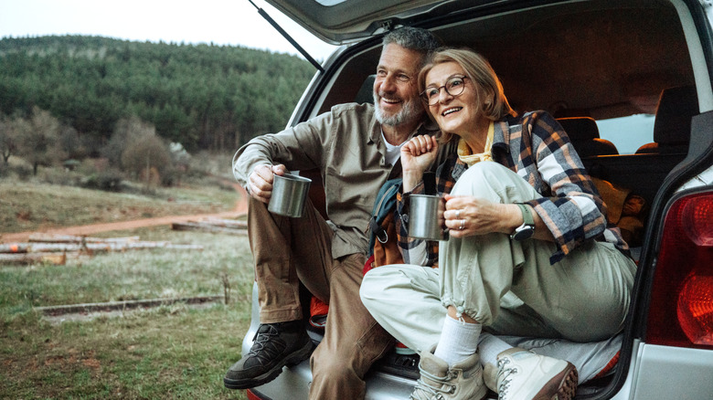 Couple camping in the back of their car, drinking from aluminum mugs