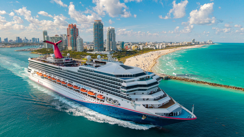 A huge Carnival Cruise Line ship departs an urban port with turquoise waters.