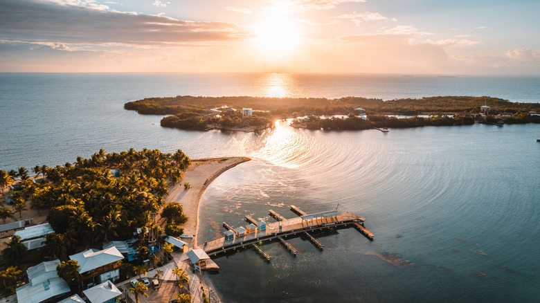 An aerial view of the beach-y Placencia coast in Belize as the sun sets in the background