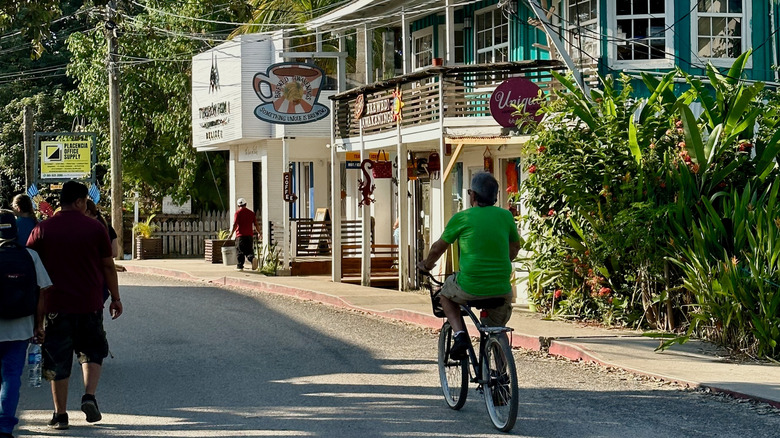 A man bicycles down a main street past small businesses on a sunny day in Placencia, Belize