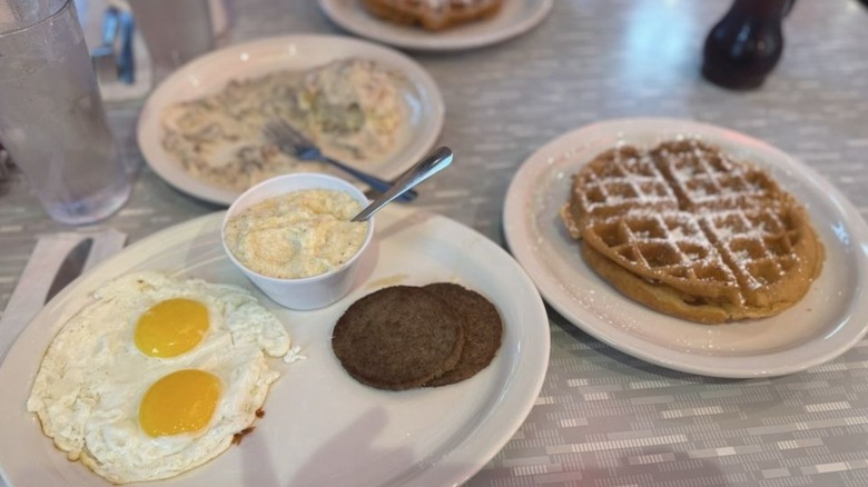 Plate with fried eggs and sausage next to plate with waffle