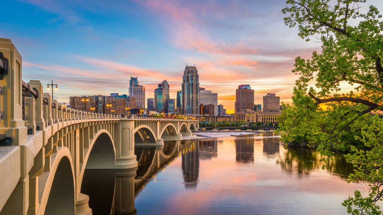 Minneapolis, Minnesota skyline at dusk with a sunset sky and large bridge leading into the city