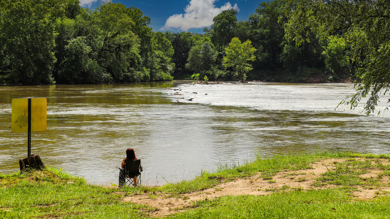 A woman sitting on the banks of the Chattahoochee River in Georgia, surrounded by lush greenery.