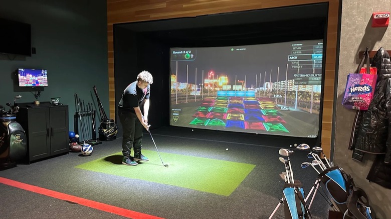 A man hitting a golf ball at the gold simulator in the TopGolf Swing Suite
