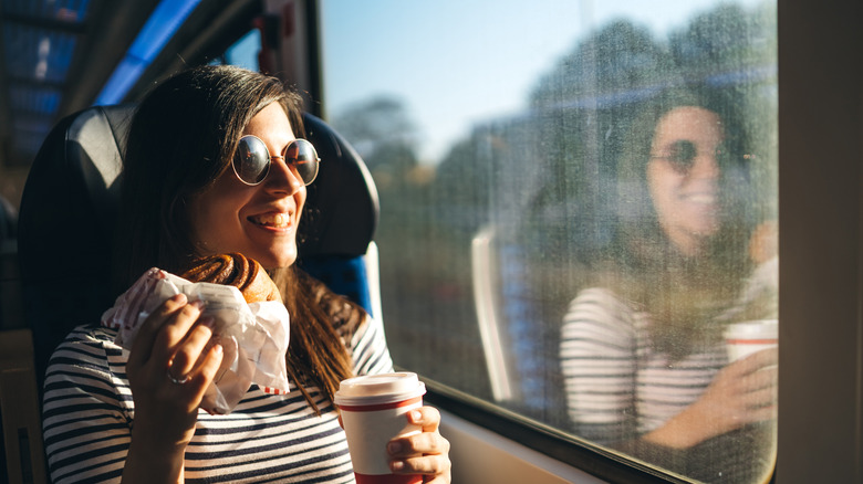 A person wearing sunglasses eating and drinking on a train