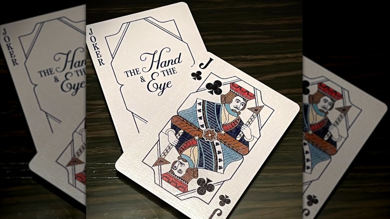 Playing cards with the jack of clubs and the Hand and the Eye branding.