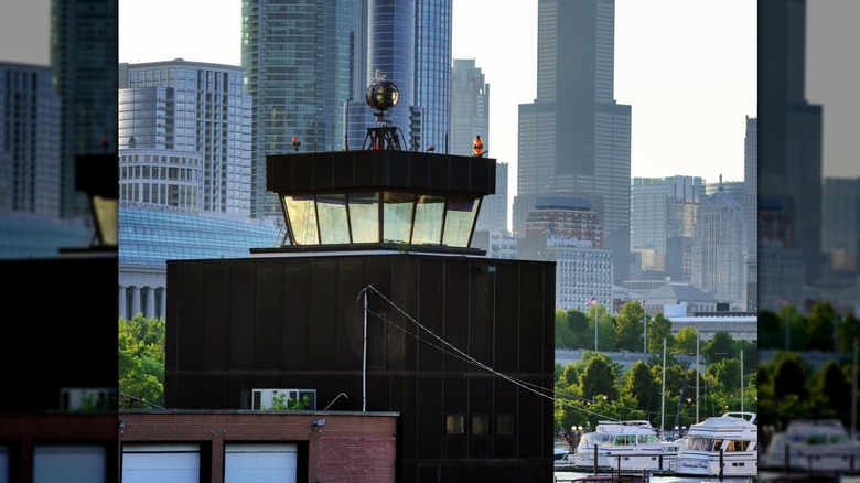 Meigs Field control tower, a blocky black building with an observation room on top, in front of the Chicago Skyline with trees and boats in the background
