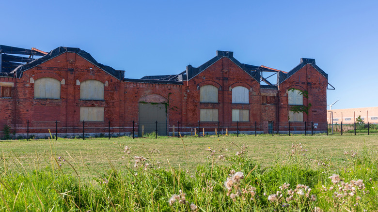 Red brick building in Pullman National Historic Park, with boarded up windows and black tarp on top, behind green grass under a blue sky