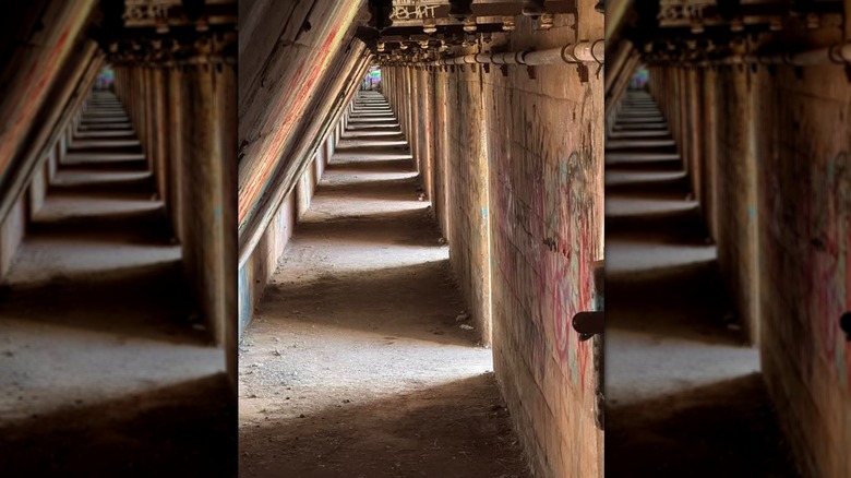 Concrete corridor inside an ore wall in Steelworkers Park, with graffiti on the walls and a pipe running along the top