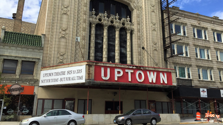 Front of the Uptown Theatre, an elaborate white brick and stone facade with a red sign reading UPTOWN and cars parked out front