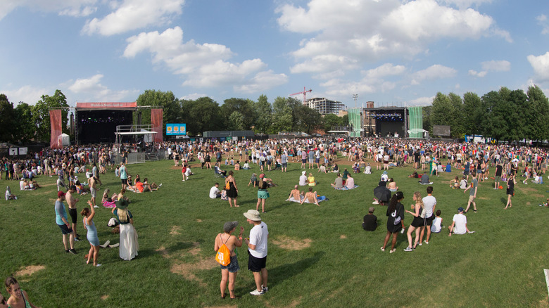 Crowd on the lawn at Union Park, with a red-draped stage on the left, a green-draped stage on the right, and trees in the background, under a cloudy blue sky