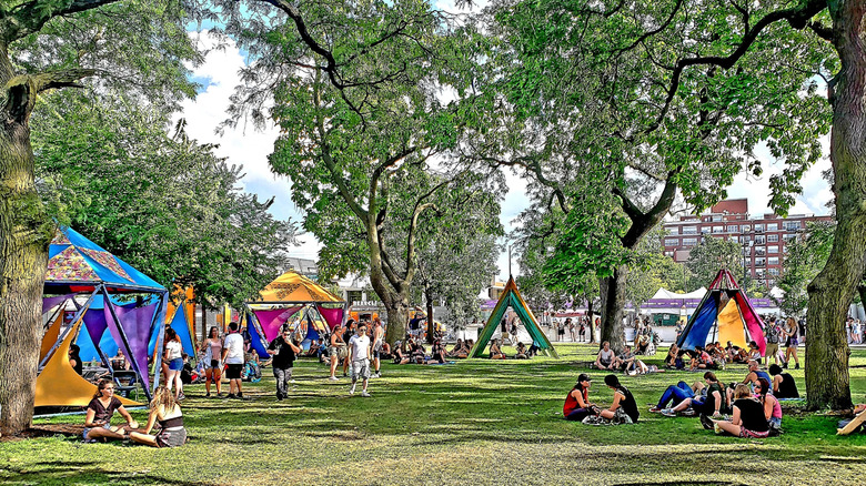 People sitting on grass and walking through a park under green trees, surrounded by colorful tents