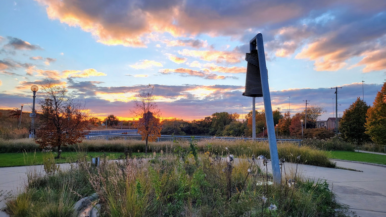 Metal statue surrounded by paved paths and grass at sunset in Palmisano Park