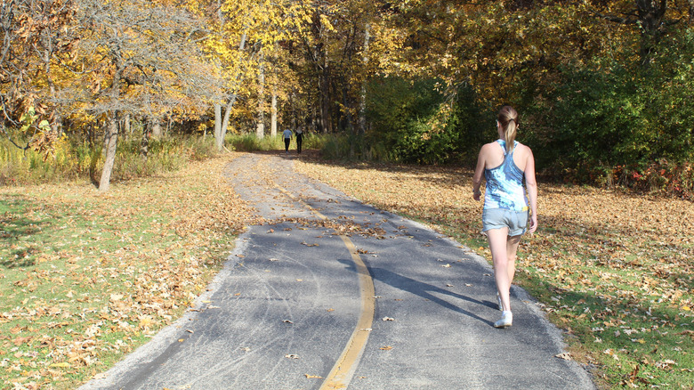 A woman walking along a paved trail through trees in Busse Woods Reservoir, Illinois