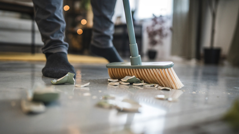 Close up of a green broom sweeping up a broken plate