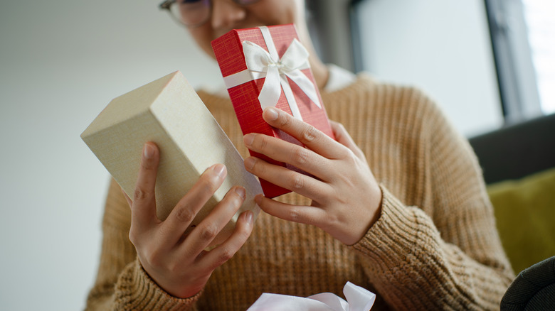 Woman in beige sweater opening a festive red and white gift box