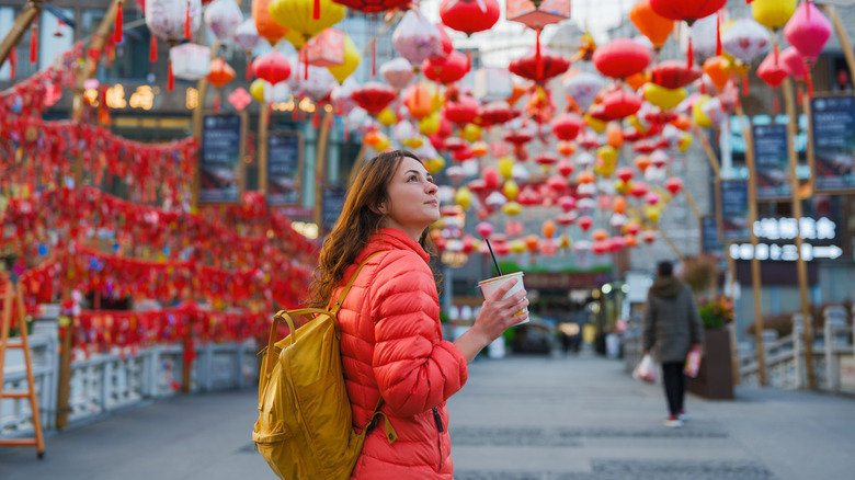 Woman in a red coat holding coffee cup under Chinese lantern decorations in Guilin, China