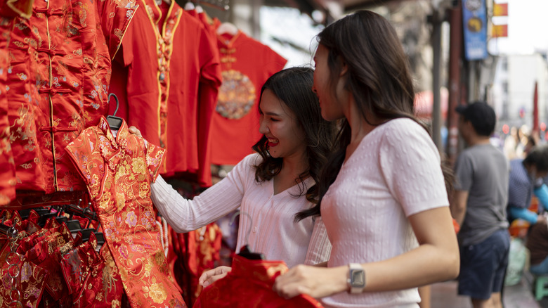 Two Asian women in an outdoor market holding red Chinese traditional clothes