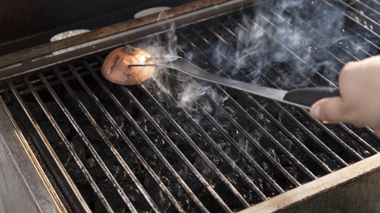 Onion half pushed onto hot grill with fork