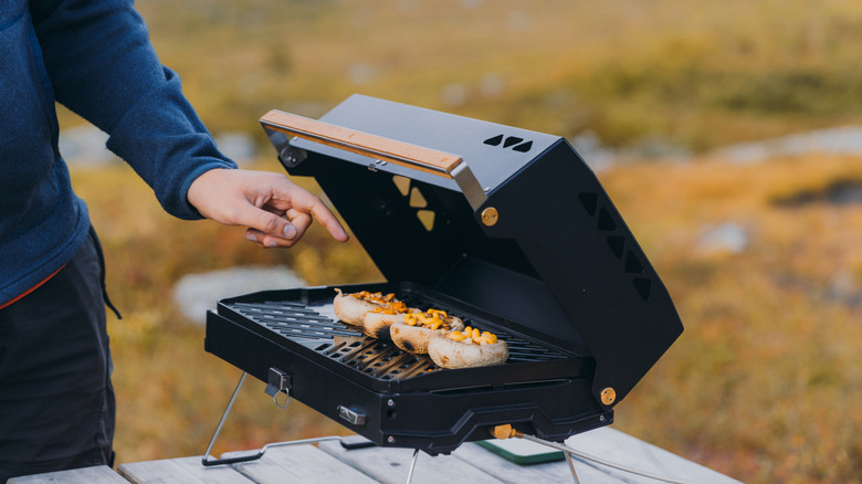 Person pointing to mushrooms on small personal grill outside