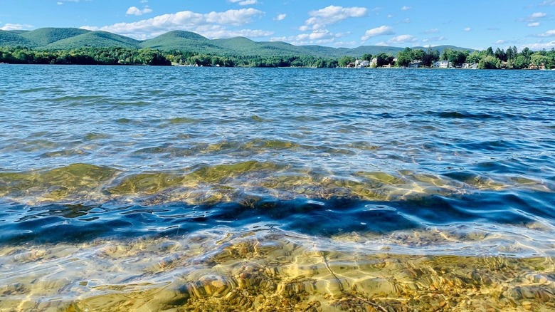 crystal clear water in a lake; the far shoreline in the background has rolling hills covered in green wooded forests